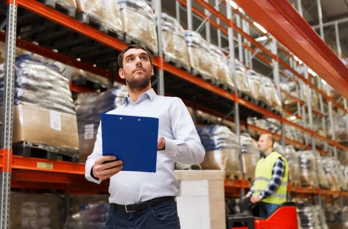 A businessman holding a clipboard inside a warehouse.